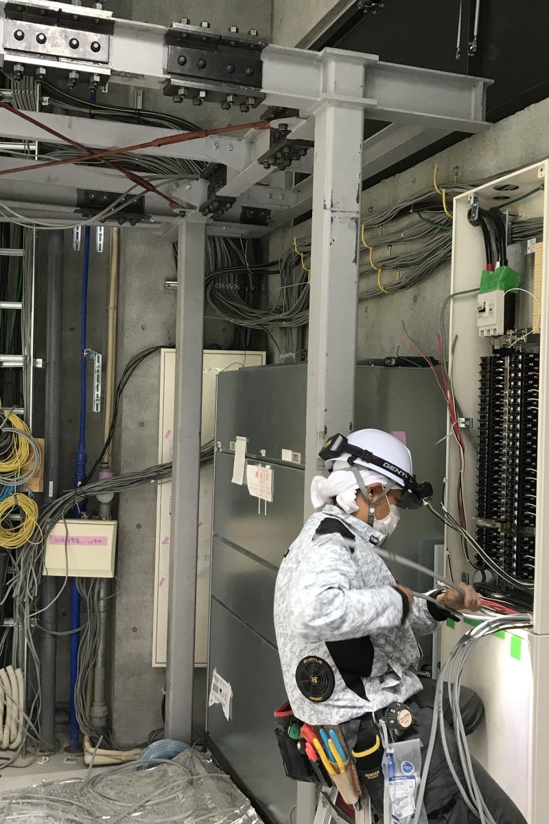 分電盤の前で配線作業をする電気工事士